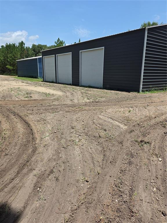 A dark metal storage building with three roll-up doors sits on a dirt lot — 00 E COUNTY ROAD 44A, EUSTIS, FL