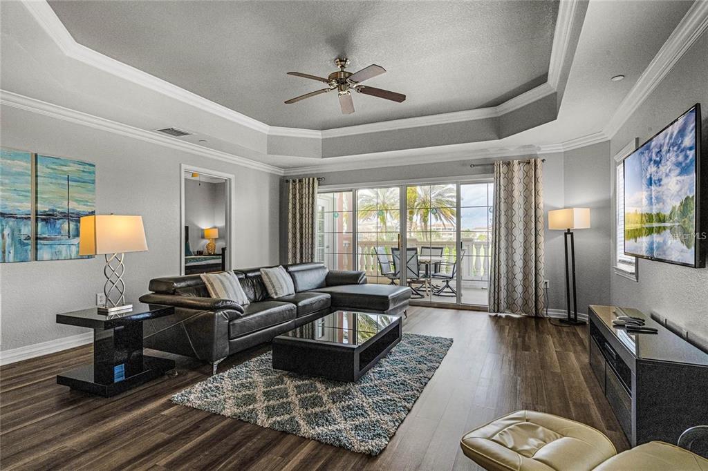 A living room with a tray ceiling, ceiling fan, and open floor plan to the kitchen — 1102 SUNSET VIEW CIRCLE UNIT 204, REUNION, FL