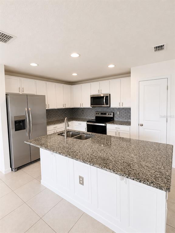 A kitchen features white cabinets, granite countertops, stainless steel appliances, and a central island — 495 TAFT DRIVE, DAVENPORT, FL