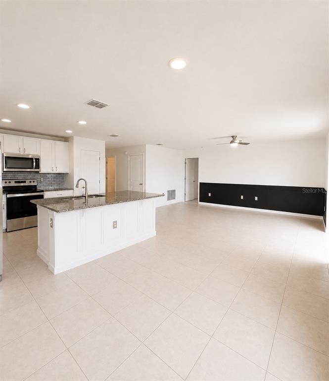 A kitchen with a granite-topped island and white cabinets opens into a large tiled room — 495 TAFT DRIVE, DAVENPORT, FL
