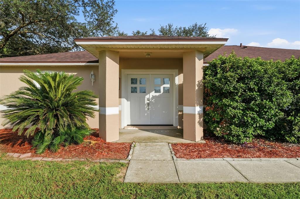 The exterior of a house features a covered entryway with double doors and landscaping — 236 COUNTRY LAKES CIRCLE, GROVELAND, FL
