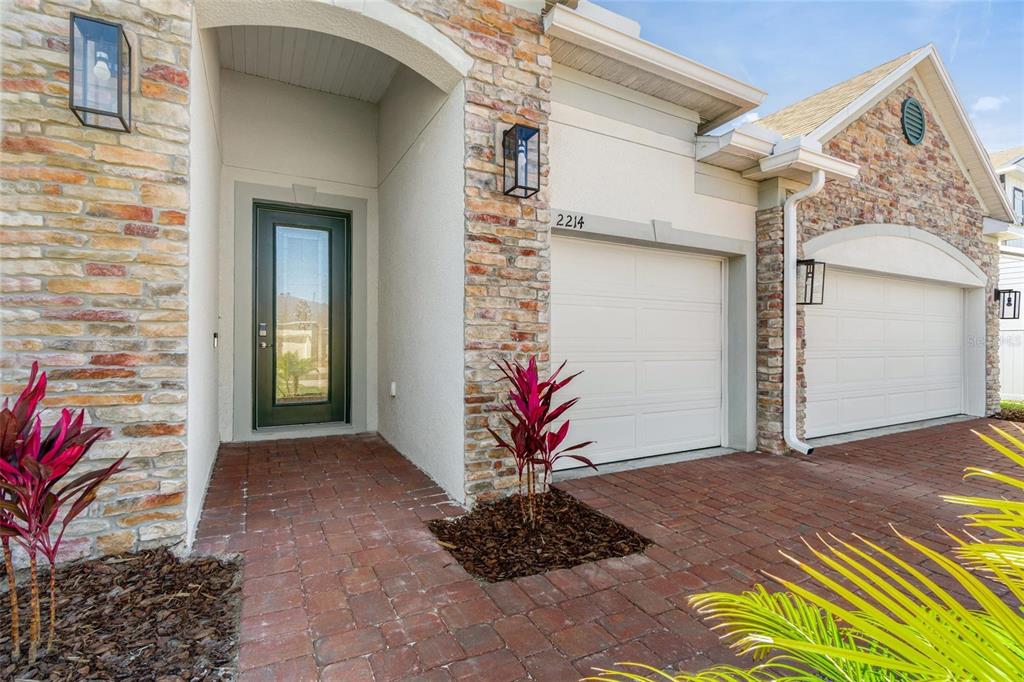 The exterior of a house features a stone facade, a brick driveway, and two garage doors — 2214 ELEGANT MANOR CIRCLE, EDGEWATER, FL