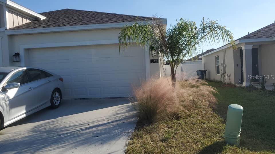 A silver sedan is parked in the driveway of a single-story house with a palm tree — 342 RUSTIC RAIL DRIVE, LAKE WALES, FL
