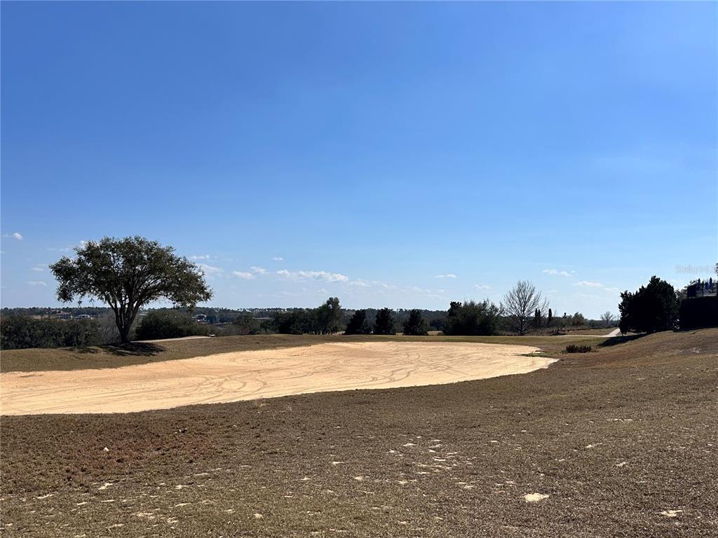 A large sand bunker sits in the foreground of a grassy, open golf course landscape — 16822 ARTIMINO LOOP, MONTVERDE, FL