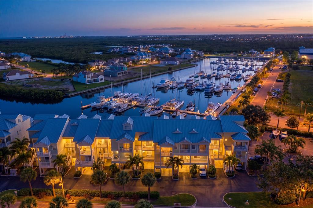 An aerial view shows a multi-story residential building with a blue roof beside a marina — 423 BAHIA BEACH BOULEVARD, RUSKIN, FL