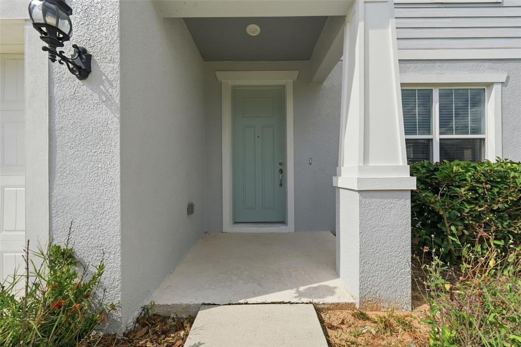 A light blue front door is set within a covered entryway with a concrete porch — 14312 CRESTAVISTA AVENUE, CLERMONT, FL
