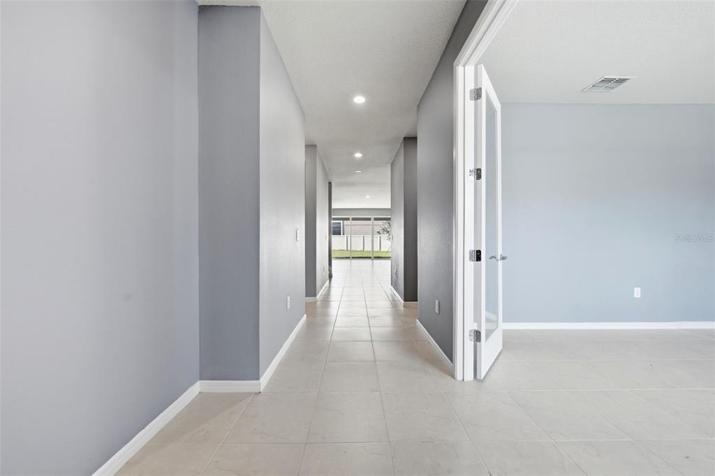 A hallway with light tile flooring leads toward a glass door overlooking a backyard — 14312 CRESTAVISTA AVENUE, CLERMONT, FL