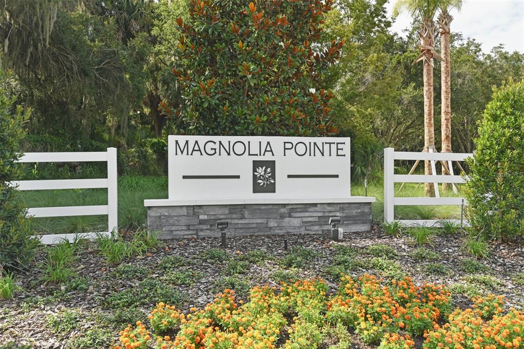 A white Magnolia Pointe community sign sits behind a bed of orange flowers — 199 BULL FROG LANE, UMATILLA, FL