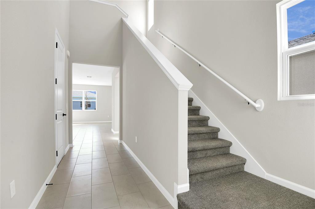 A foyer with tile flooring features a carpeted staircase and a view into another room — 199 BULL FROG LANE, UMATILLA, FL