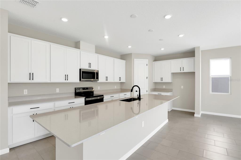 A modern kitchen features white cabinetry, a large quartz island, and stainless steel appliances — 199 BULL FROG LANE, UMATILLA, FL