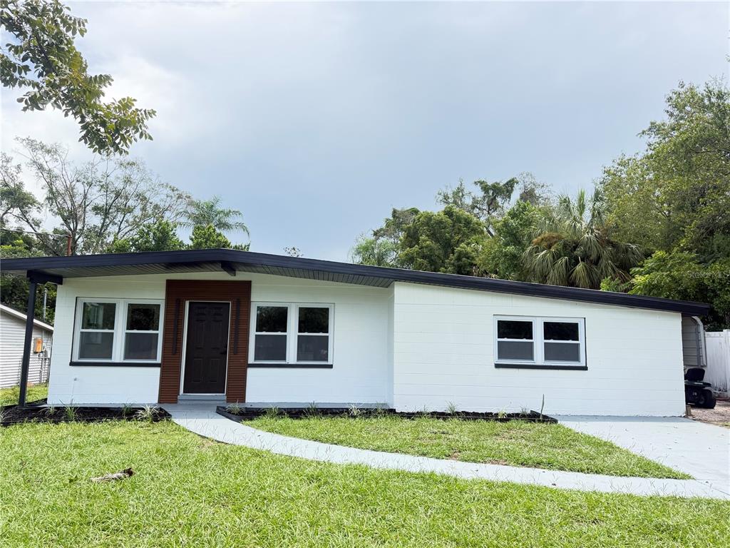 A single-story white house with a dark roof, wood-paneled entryway, and a concrete walkway — 9505 N WILLOW AVENUE, TAMPA, FL