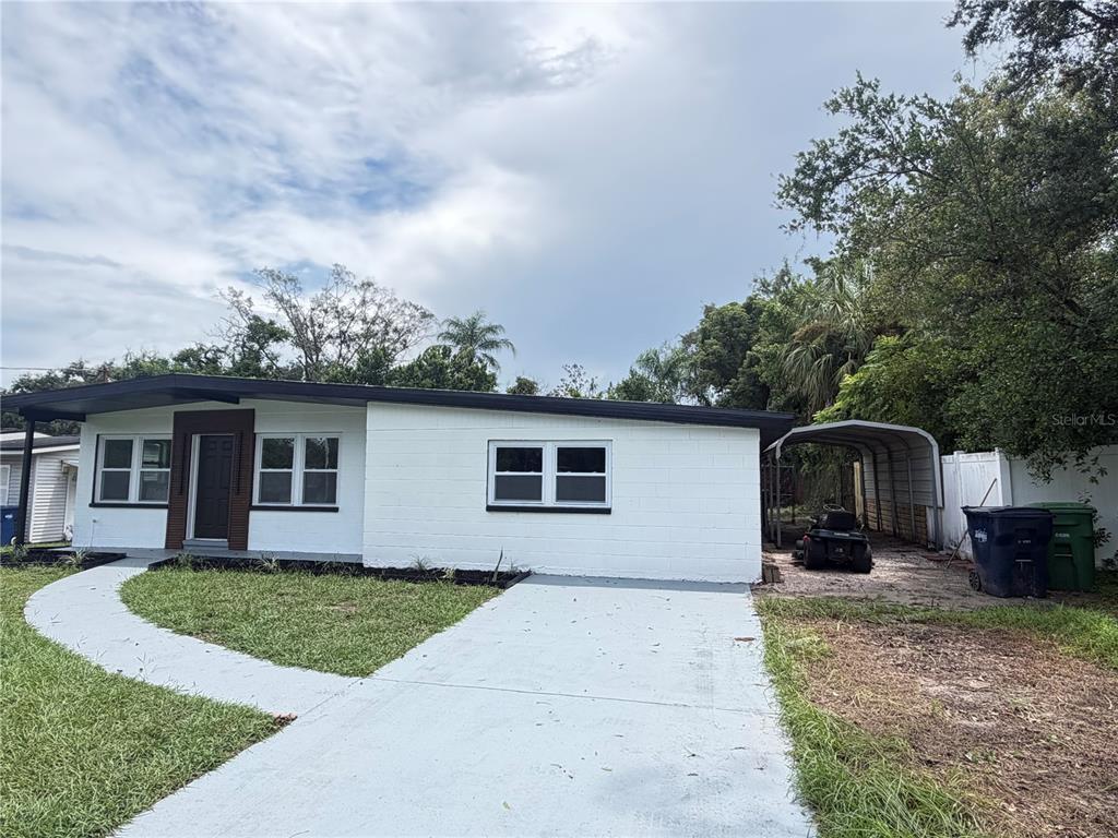 A single-story white concrete block house features a dark roof, a carport, and a paved walkway — 9505 N WILLOW AVENUE, TAMPA, FL