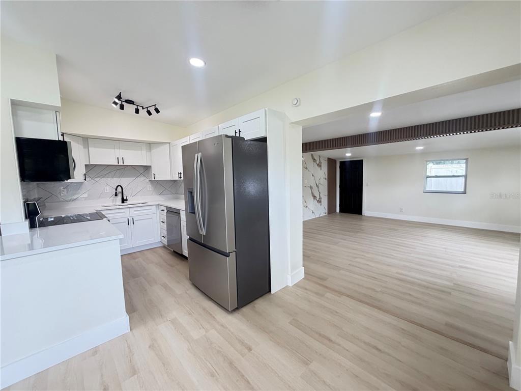 A modern kitchen with white cabinets and stainless steel appliances opens into a living area — 9505 N WILLOW AVENUE, TAMPA, FL