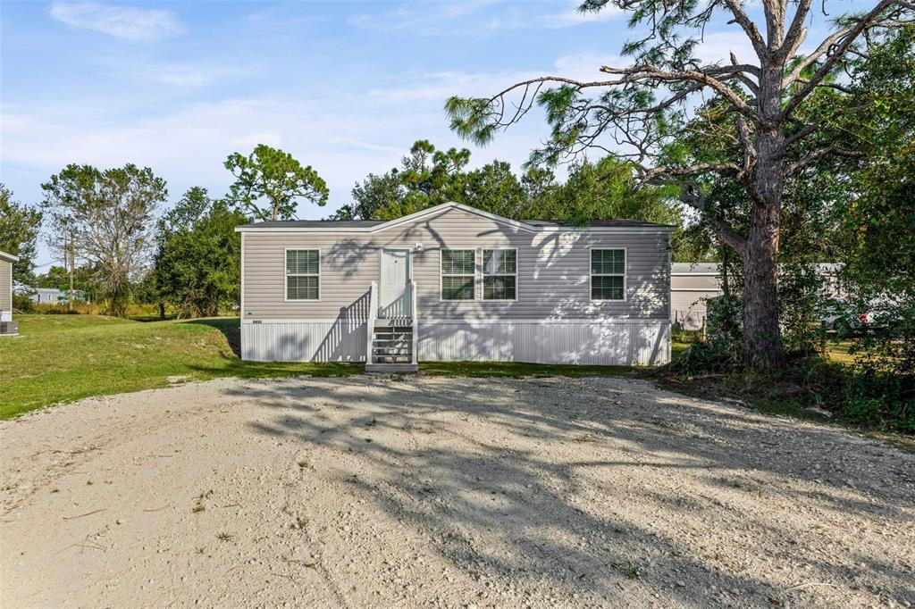 A light gray manufactured home sits on a gravel lot surrounded by trees — 8432 SWEDEN BOULEVARD, PUNTA GORDA, FL