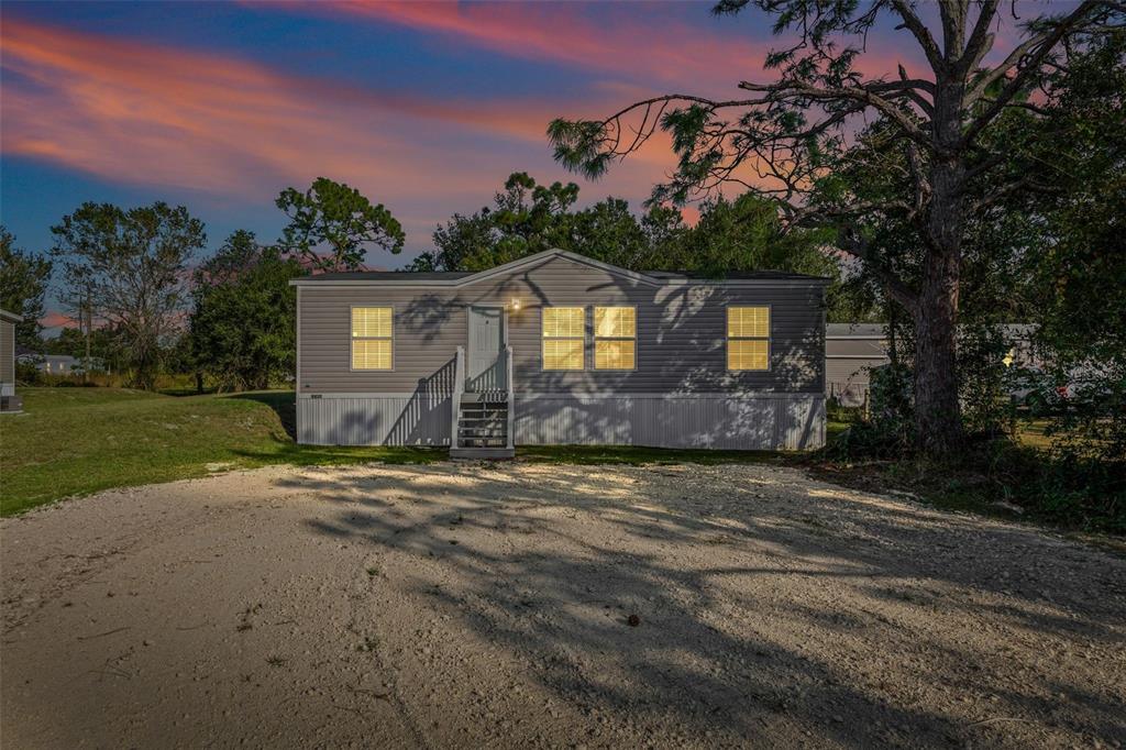 A single-story manufactured home with gray siding sits behind a gravel driveway at sunset — 8432 SWEDEN BOULEVARD, PUNTA GORDA, FL