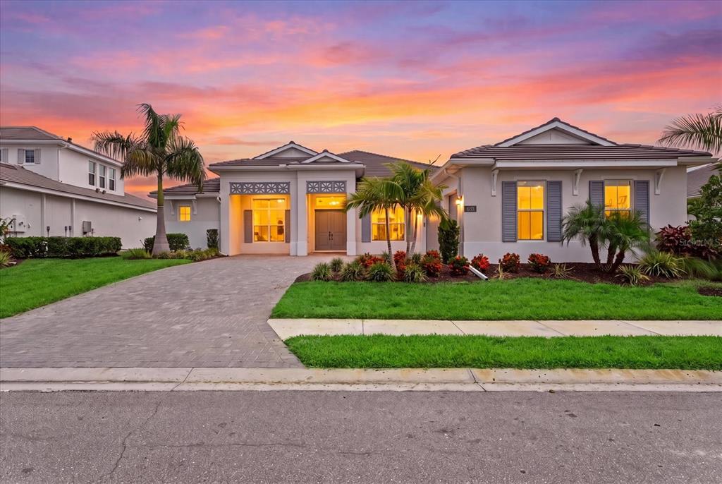 A single-story house with a paved driveway, palm trees, and a sunset sky — 8133 NEVIS RUN, LAKEWOOD RANCH, FL