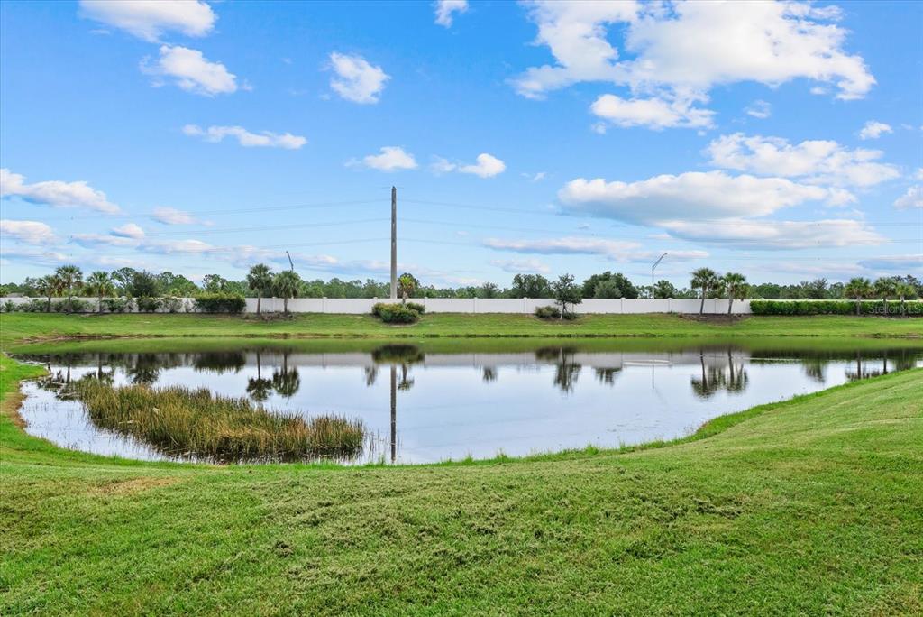A grassy lawn slopes down toward a retention pond with a white fence in back — 8133 NEVIS RUN, LAKEWOOD RANCH, FL