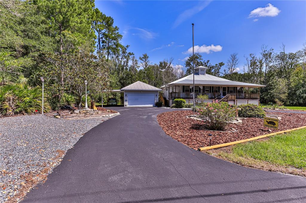 A paved driveway leads to a detached garage and a house with a wrap-around porch — 11071 W THOREAU PLACE, CRYSTAL RIVER, FL