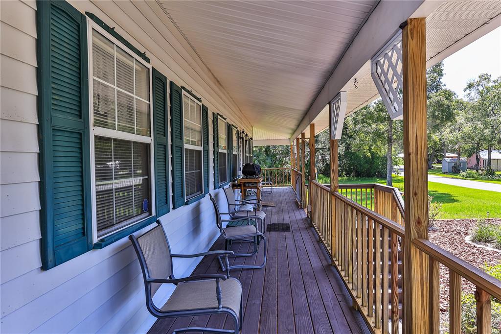 A long wooden porch features a railing, outdoor chairs, and green shutters on the house — 11071 W THOREAU PLACE, CRYSTAL RIVER, FL