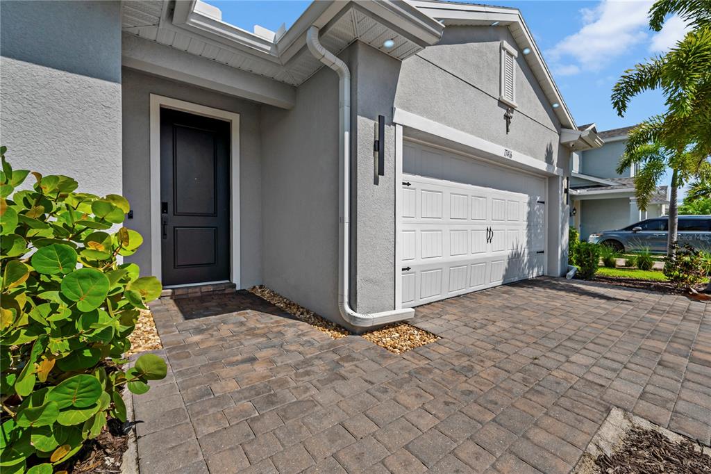 The exterior of a house features a gray stucco facade, a white garage door, and pavers — 17416 SILVERSPUR DRIVE, PUNTA GORDA, FL
