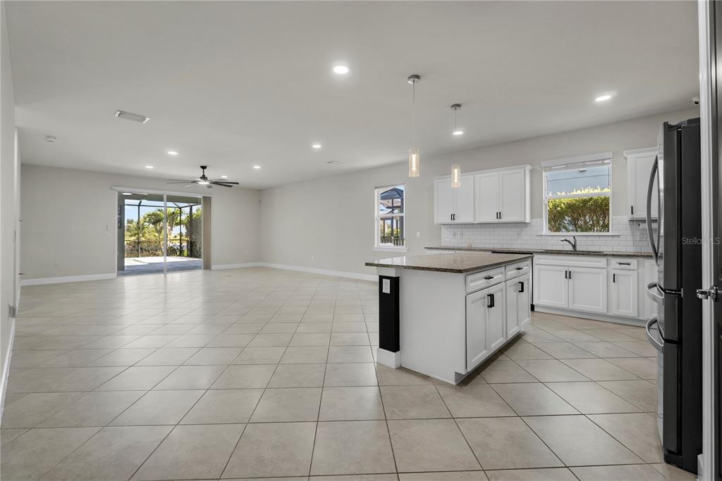 An open-concept kitchen and living area with white cabinets, a granite island, and tile flooring — 17416 SILVERSPUR DRIVE, PUNTA GORDA, FL