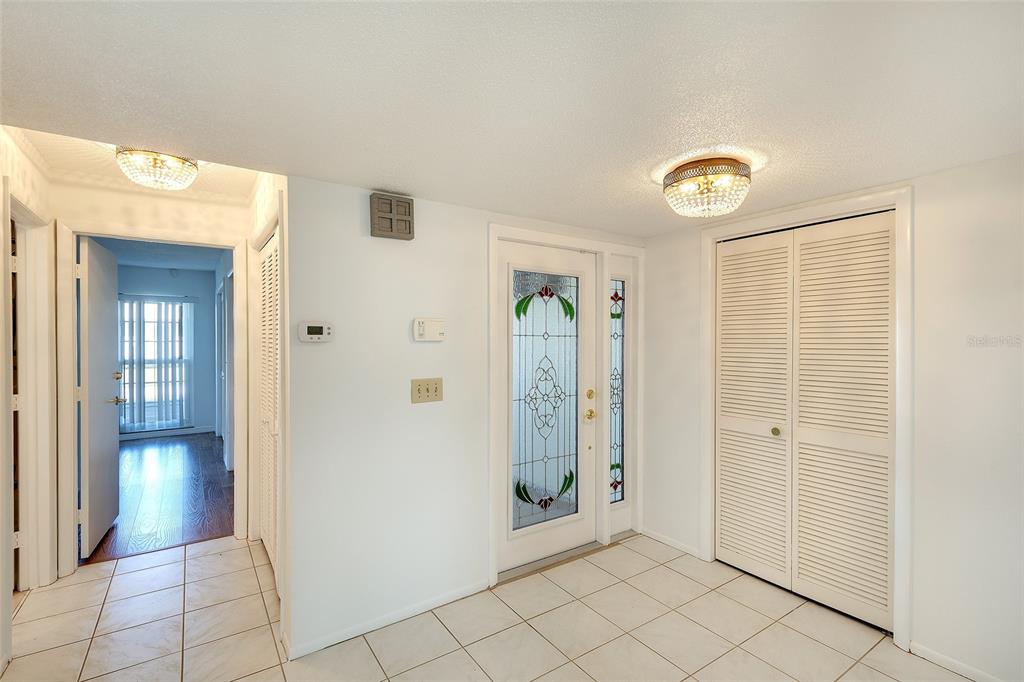 An entryway with white tile flooring, a glass-paneled front door, and a louvered closet door — 6517 10TH AVENUE W, BRADENTON, FL