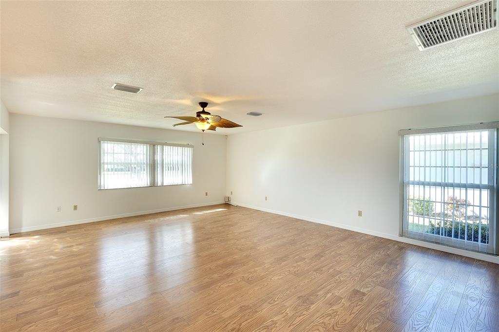 An empty living room features light wood-look flooring, white walls, and a ceiling fan — 6517 10TH AVENUE W, BRADENTON, FL