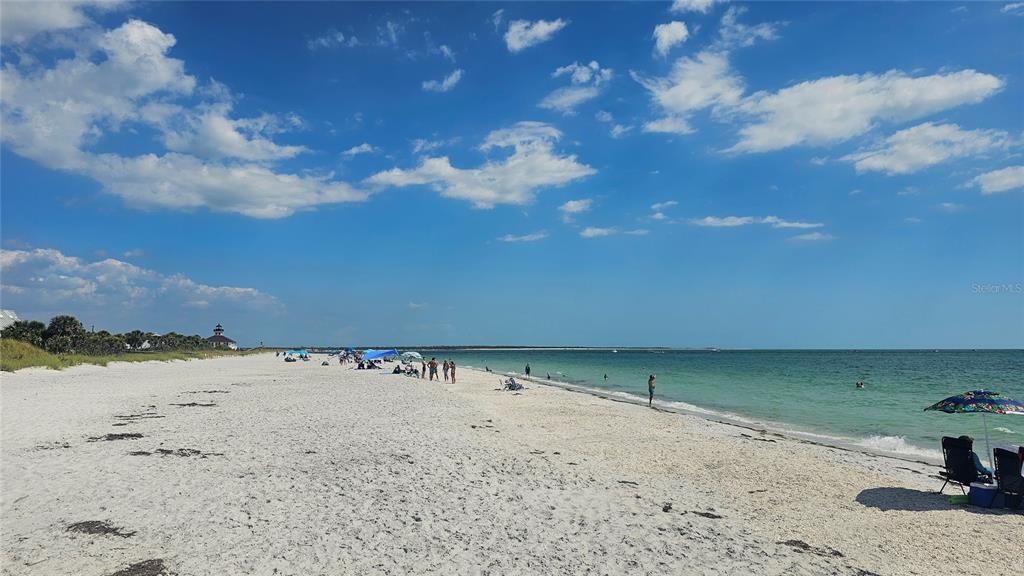 A wide, sandy beach with people, umbrellas, and a distant lighthouse under a blue sky — 12043 BACCHUS ROAD, PORT CHARLOTTE, FL