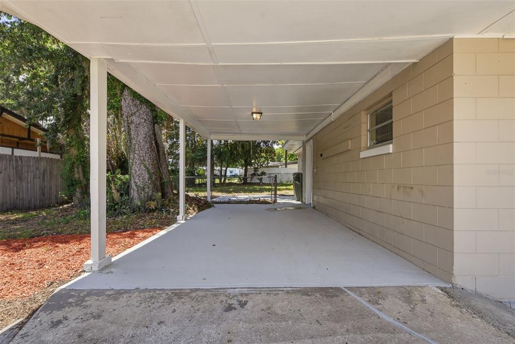 A concrete carport with a white metal roof attached to a tan block house — 509 SCENIC STREET, LEESBURG, FL