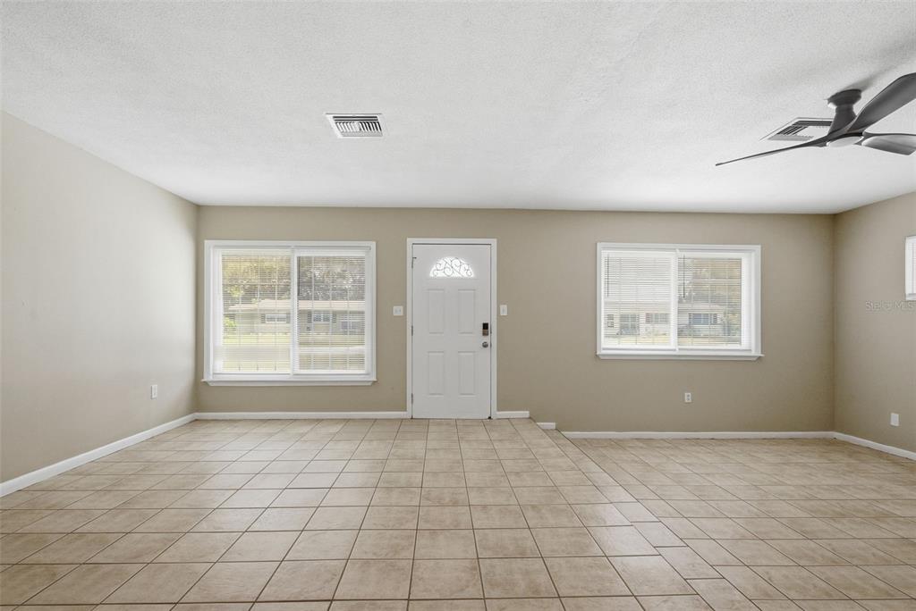 An empty room with beige walls, tile flooring, a white front door, and two windows — 509 SCENIC STREET, LEESBURG, FL