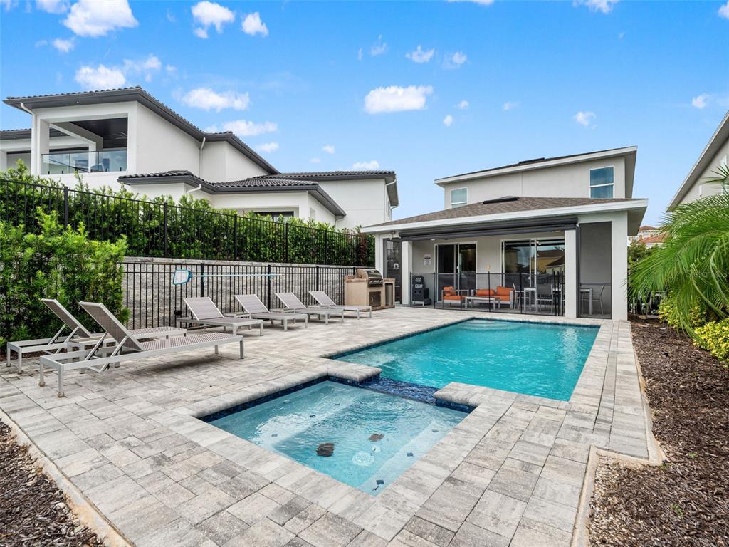 A backyard features a swimming pool, a spa, lounge chairs, and a covered patio area — 1407 TITIAN COURT, KISSIMMEE, FL