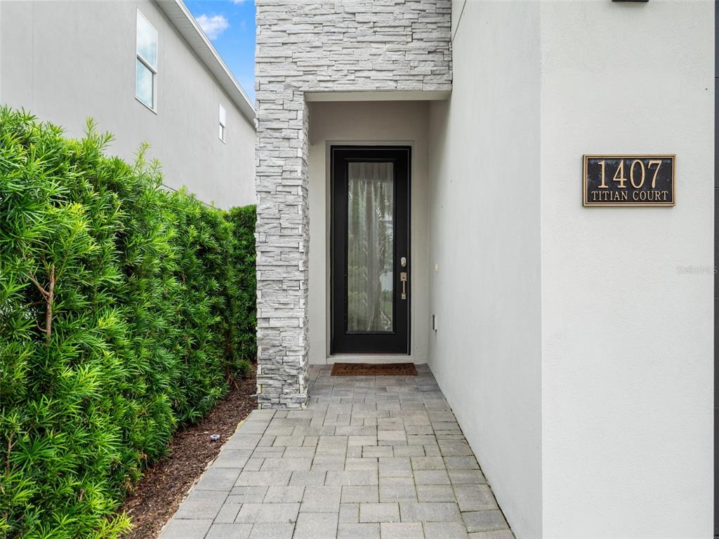 A stone-accented entryway leads to a black-framed glass front door on a paved walkway — 1407 TITIAN COURT, KISSIMMEE, FL