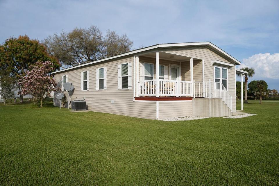 A tan manufactured home with a front porch and white railings sits on a lawn — 56 MANOR DRIVE, FORT PIERCE, FL