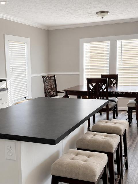 A kitchen island with a black countertop and three upholstered stools faces a dining area — 56 MANOR DRIVE, FORT PIERCE, FL