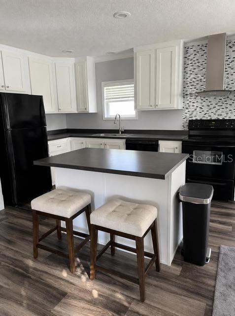 A kitchen features white cabinets, a dark island with two stools, and black appliances — 56 MANOR DRIVE, FORT PIERCE, FL