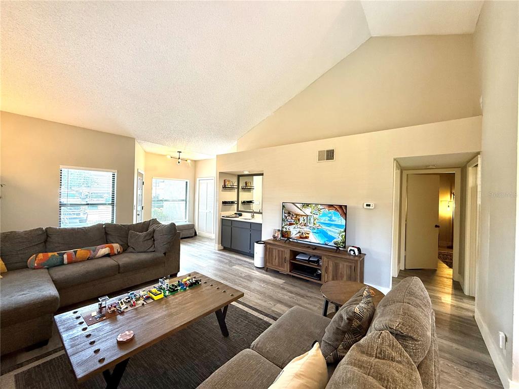 A living room features a vaulted ceiling, a black tiled fireplace, and two gray sofas — 2816 COUNTRYBROOK DRIVE UNIT L16, PALM HARBOR, FL