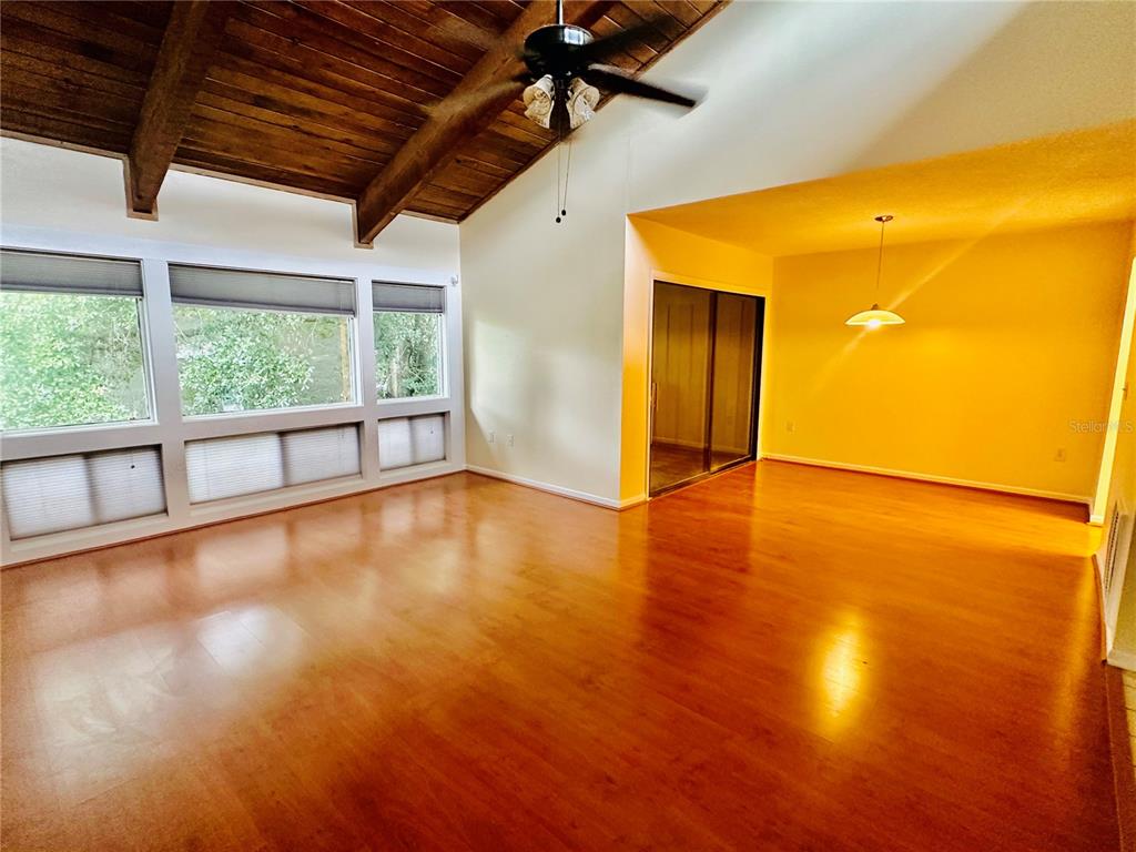A living room features vaulted wood-beamed ceilings, hardwood flooring, and large windows — 6057 WINDHOVER DRIVE UNIT E-08, ORLANDO, FL