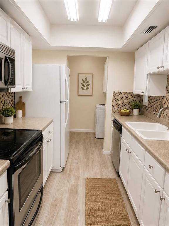 A galley kitchen features white cabinets, stainless steel appliances, and a laundry area beyond — 6057 WINDHOVER DRIVE UNIT E-08, ORLANDO, FL
