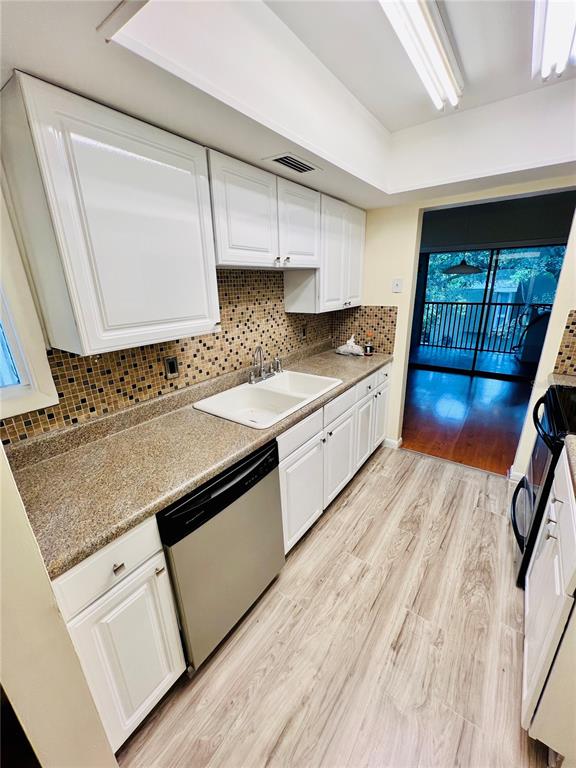 A kitchen features white cabinets, a speckled countertop, a stainless dishwasher, and wood-look flooring — 6057 WINDHOVER DRIVE UNIT E-08, ORLANDO, FL