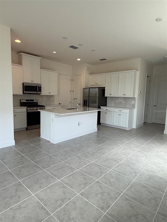 A kitchen with white cabinets, stainless steel appliances, a center island, and gray tile flooring — 2315 DATURA LOOP, ST CLOUD, FL