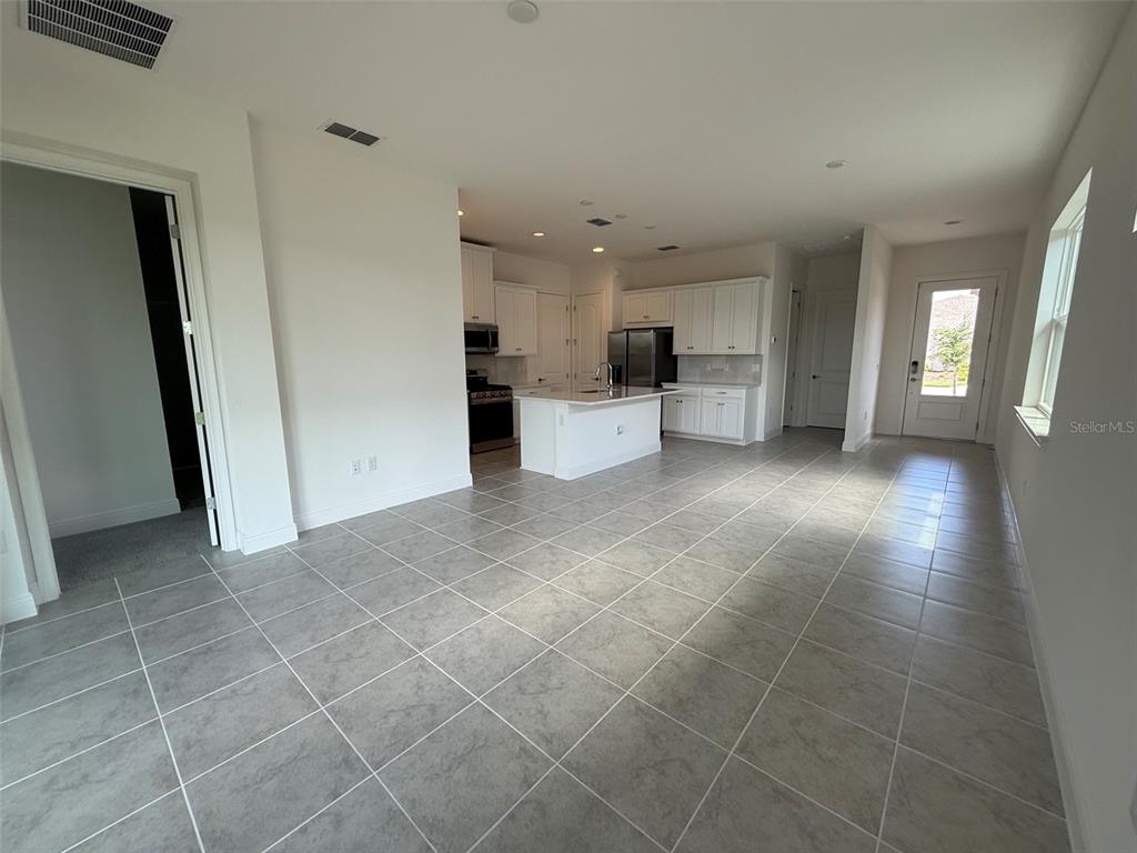 An open-concept kitchen with white cabinets and a central island features light-colored tile flooring — 2315 DATURA LOOP, ST CLOUD, FL