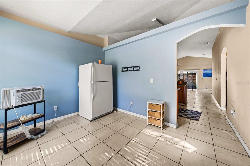 A kitchen area features a white refrigerator, a window air conditioner, and light-colored tile flooring — 7865 PINE FORK DRIVE, ORLANDO, FL