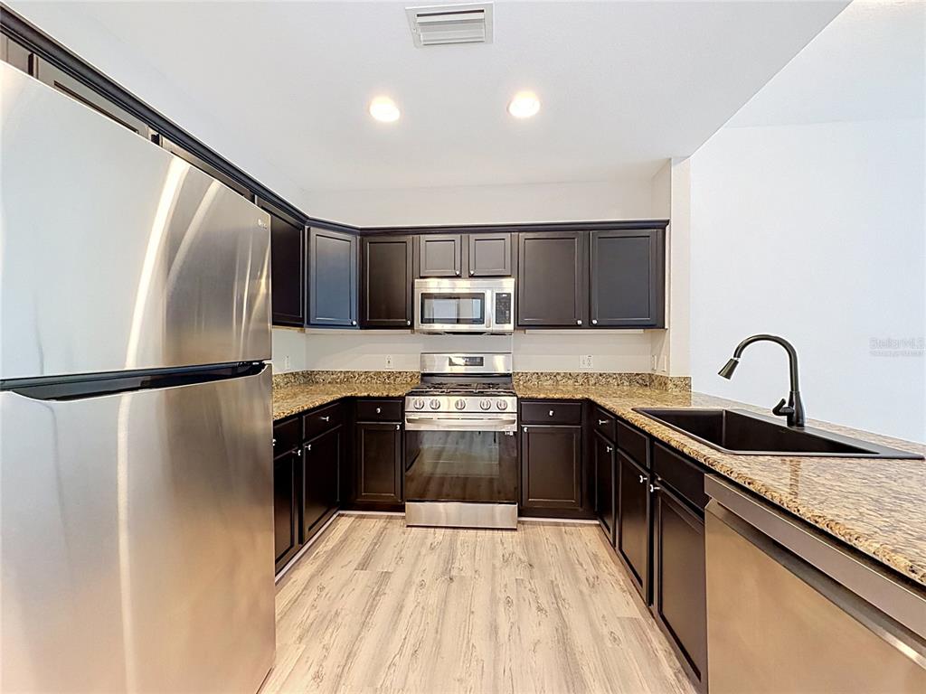 A kitchen features dark wood cabinets, stainless steel appliances, and granite countertops — 7510 SEVEN EAGLES WAY, KISSIMMEE, FL