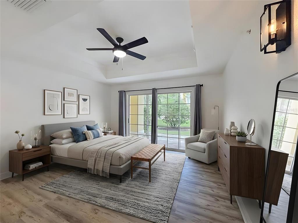 A modern bedroom features a tray ceiling, wood-look flooring, a bed, and sliding glass doors — 7510 SEVEN EAGLES WAY, KISSIMMEE, FL