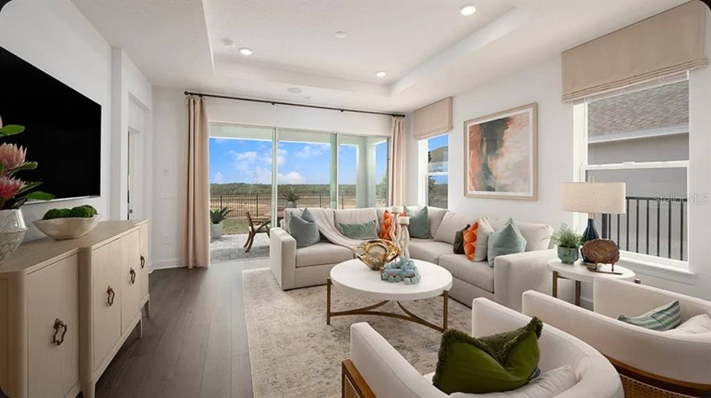 A bright living room features a large sectional sofa, white coffee table, and sliding glass doors — 11202 SILVER TRUMPET LOOP, WINTER GARDEN, FL