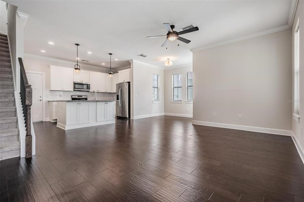An open-concept kitchen and living area features dark wood floors, white cabinetry, and stairs — 845 AURORA WAY, OLDSMAR, FL