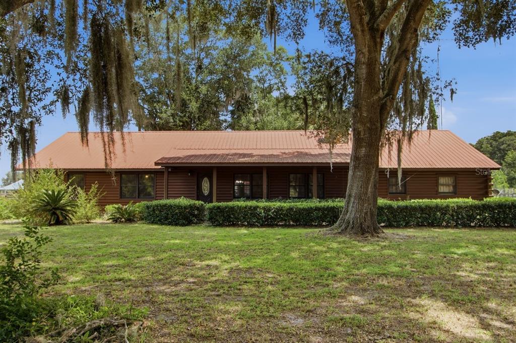 A single-story log cabin home features a metal roof, a front porch, and mature trees — 2259 BROWNLEE ROAD, SEVILLE, FL