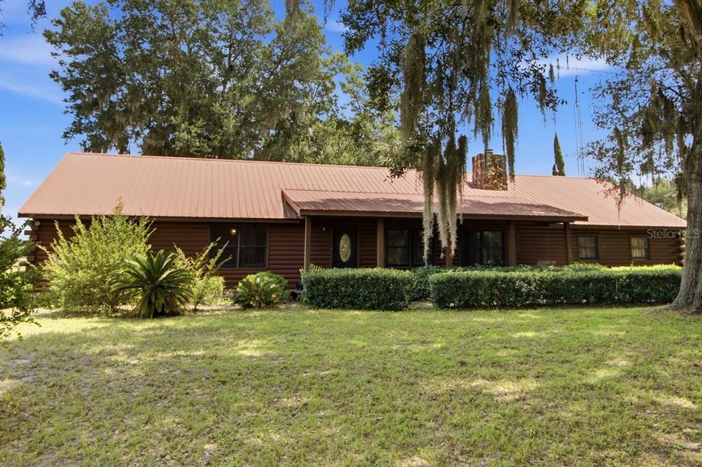 A single-story log cabin home features a metal roof and a stone chimney — 2259 BROWNLEE ROAD, SEVILLE, FL