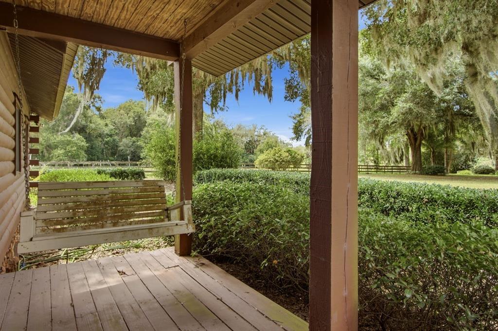 A wooden porch features a hanging bench swing overlooking a green yard with mature trees — 2259 BROWNLEE ROAD, SEVILLE, FL
