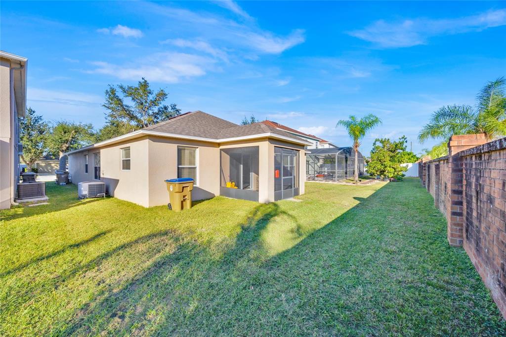 A backyard view of a house with a screened-in patio and a brick wall — 4647 CAVERNS DRIVE, KISSIMMEE, FL